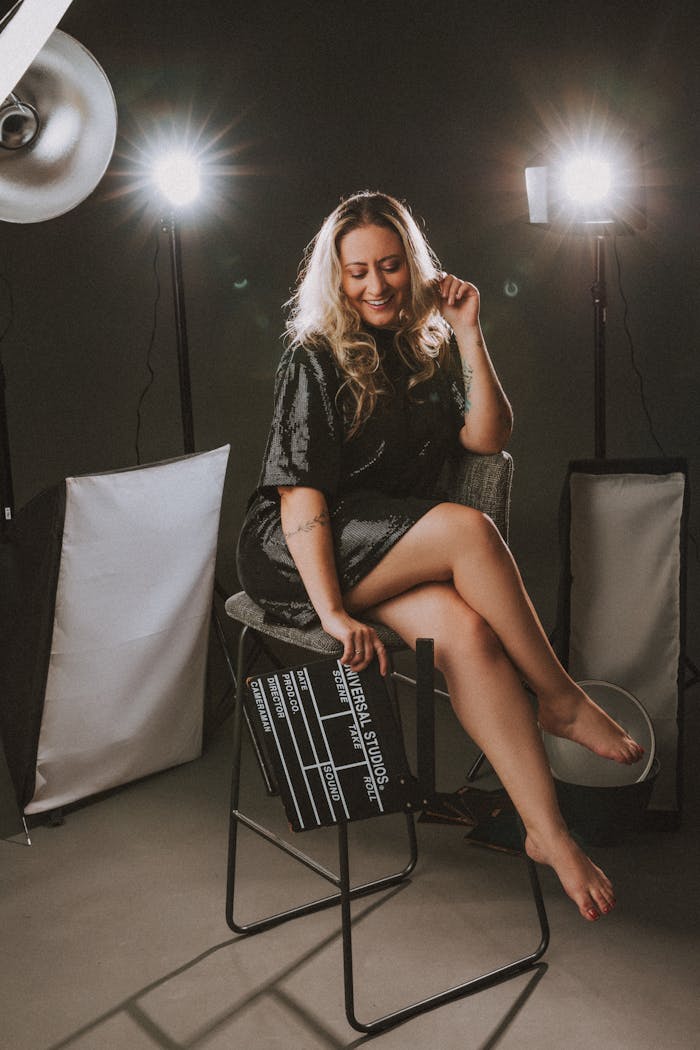 Woman posing barefoot in a studio setup holding a clapperboard.