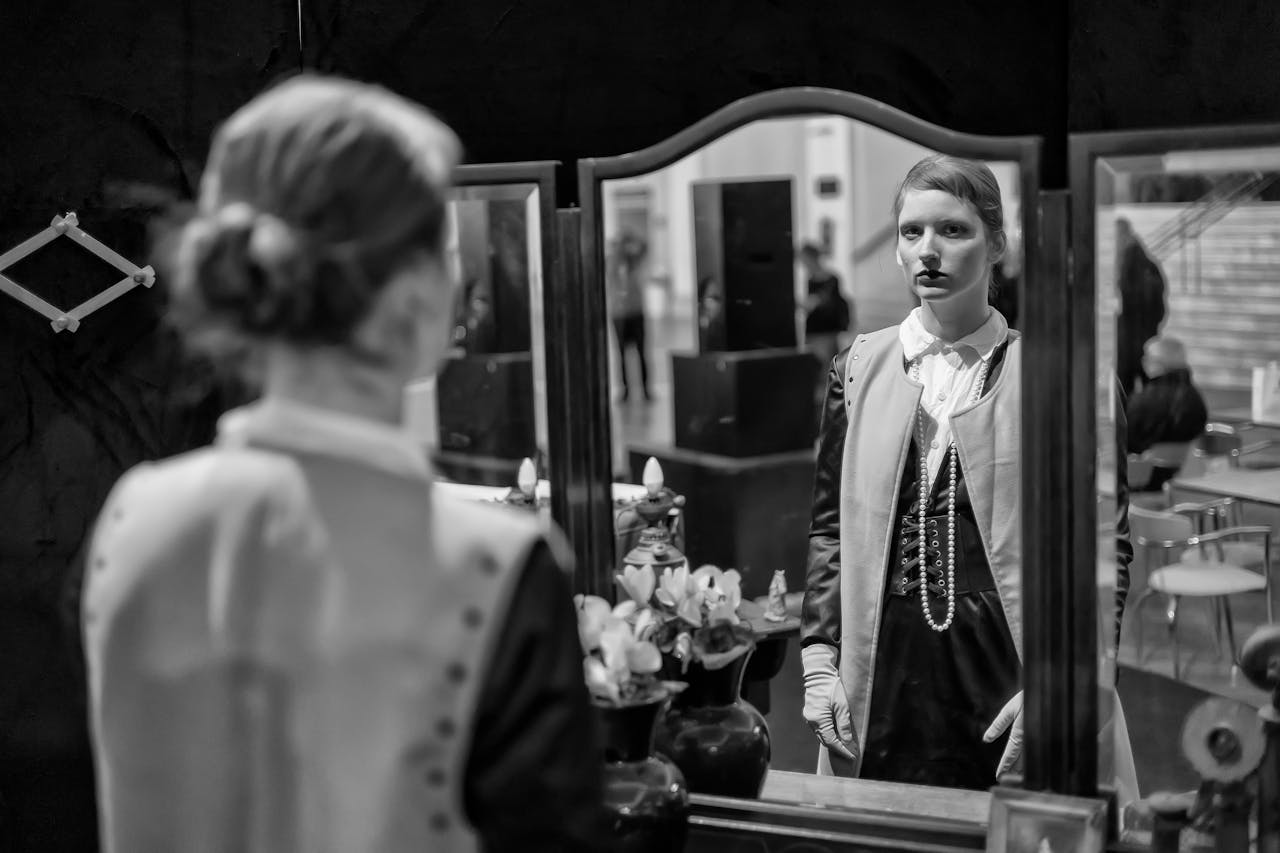 A woman in costume gazes into a mirror, capturing her reflection in an artistic setting.